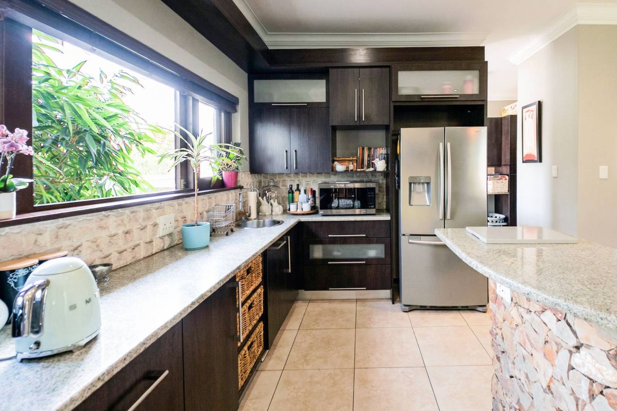 A well-appointed kitchen featuring dark wood cabinetry, granite countertops, a stone-clad breakfast bar, and large windows overlooking the garden.