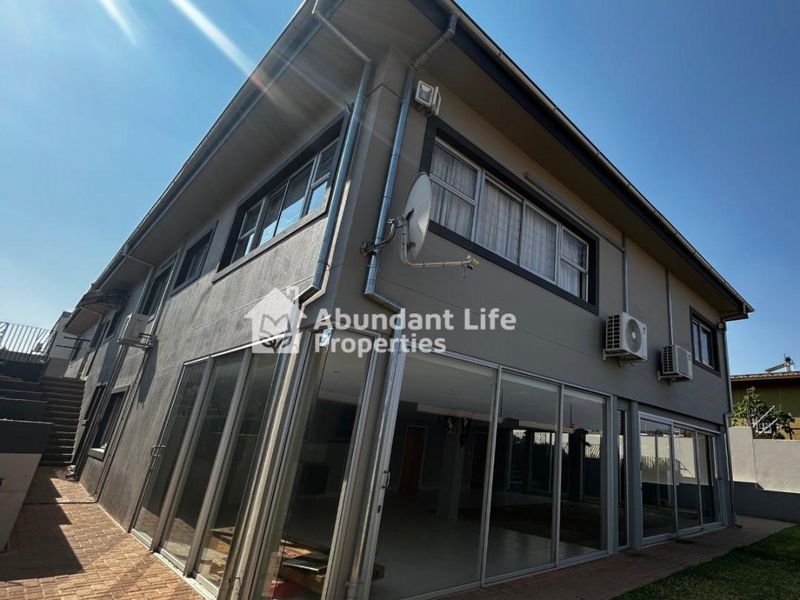 Rear exterior view of a multi-story house featuring large sliding glass doors, paved patio area, and external air conditioning units.