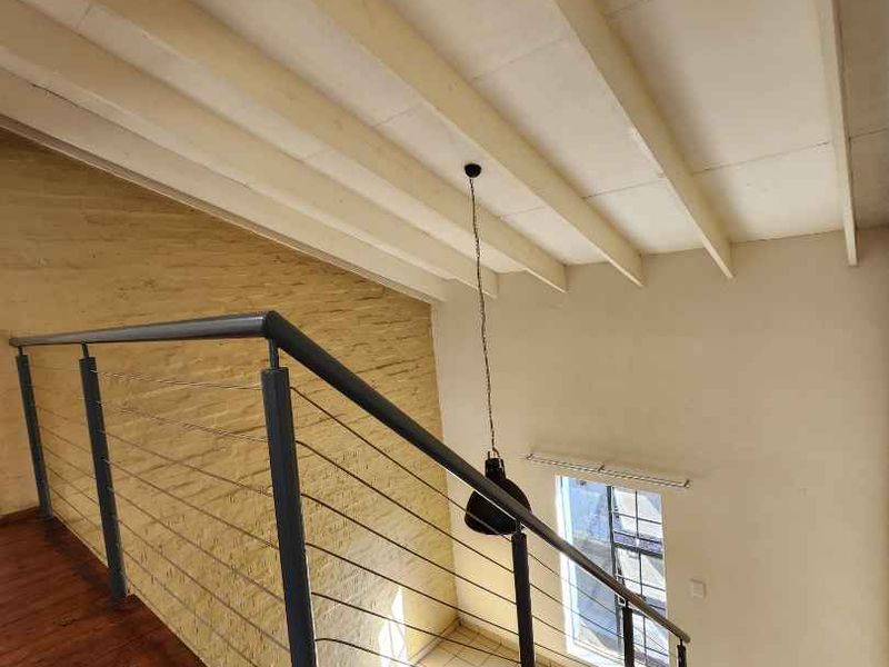 A bright hallway featuring a timber staircase with a modern metal balustrade, exposed ceiling beams, and a textured feature wall.