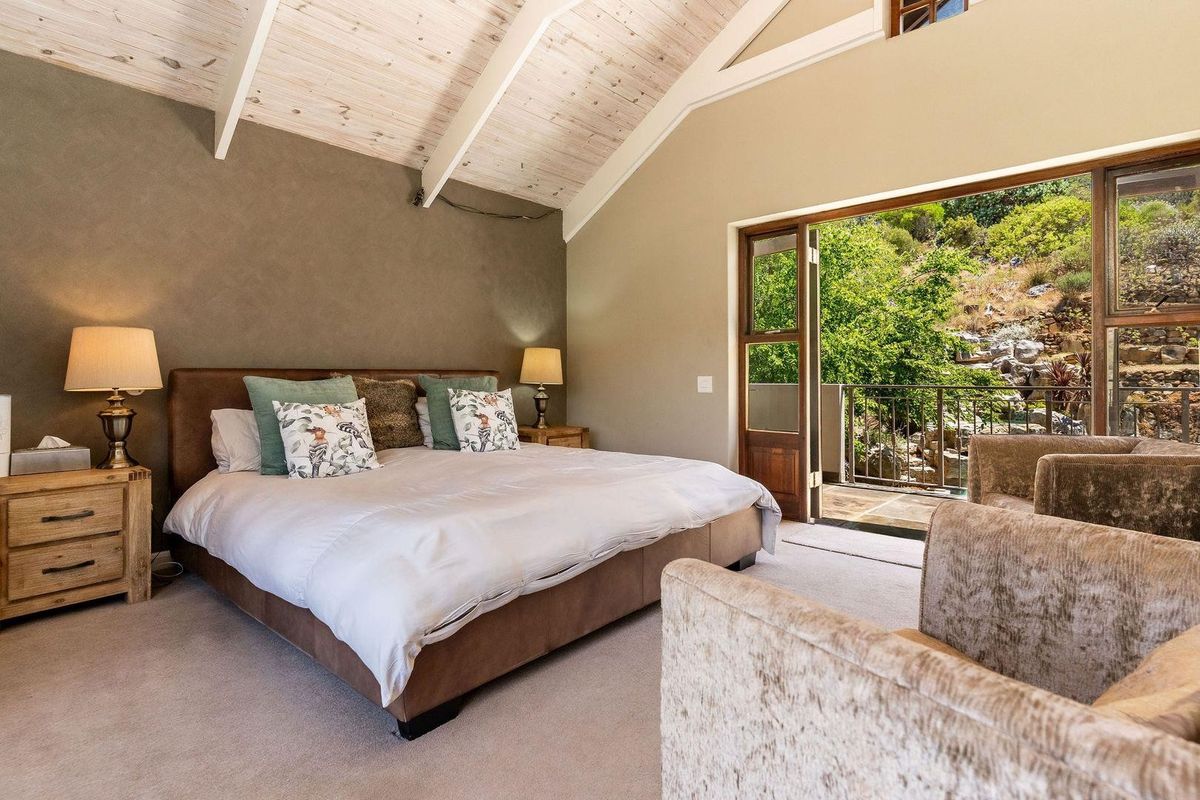 Spacious bedroom featuring vaulted timber-clad ceilings, neutral wall finishes, and direct access to a private balcony with scenic outdoor views.