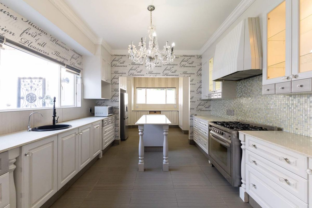 A well-appointed kitchen featuring white shaker cabinetry, stone countertops, a central island, gas range with extractor, and a decorative mosaic tile backsplash.
