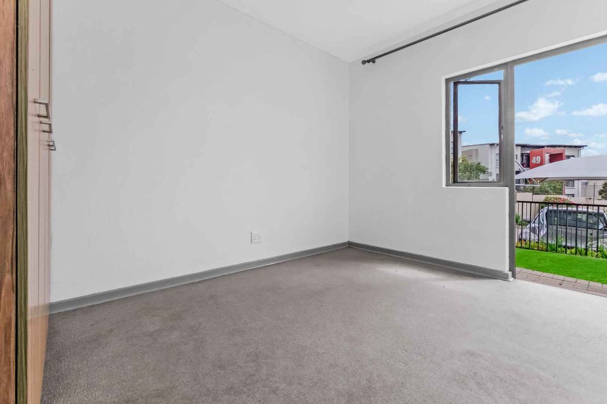 A bright, empty bedroom featuring neutral carpeting, built-in cupboards, and a glass door providing access to an outdoor balcony area.