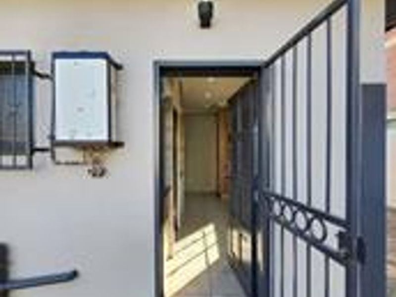Exterior view of the apartment entrance featuring a security gate, wall-mounted gas geyser, and exterior lighting.