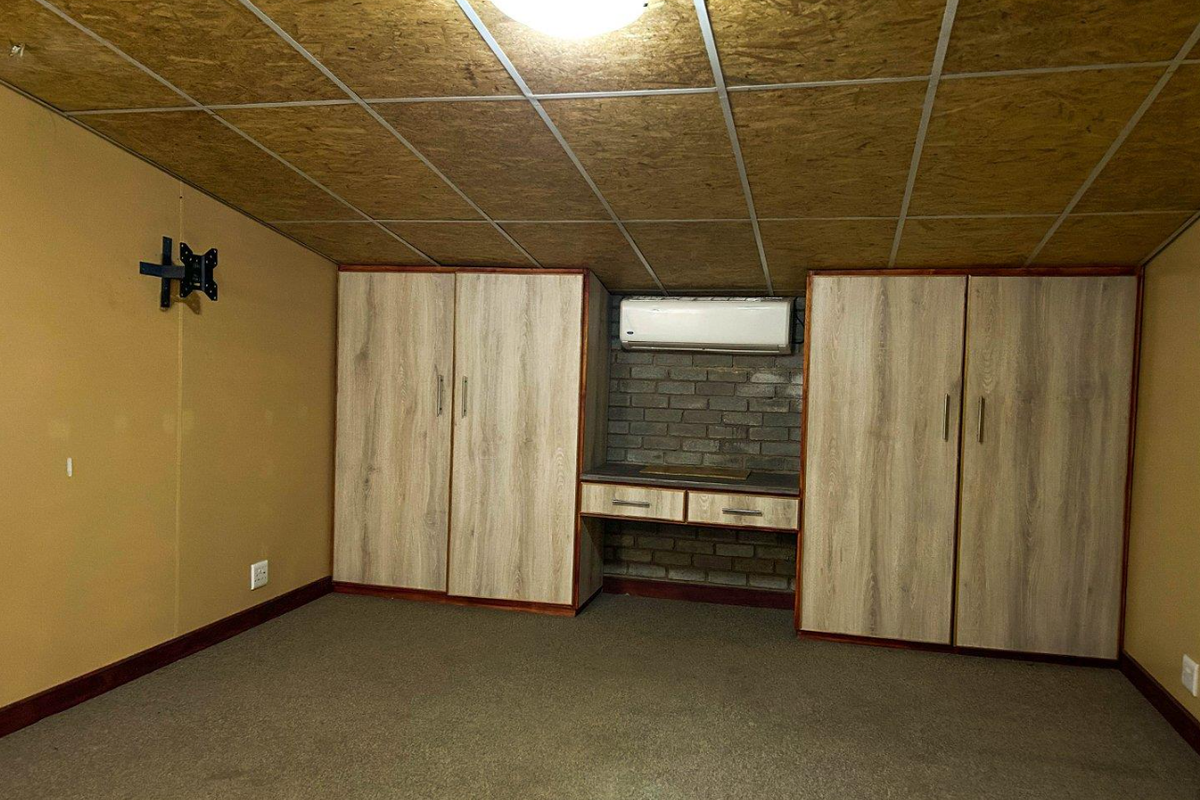 An empty bedroom featuring built-in cupboards, an air conditioning unit, and an exposed brick accent wall under a suspended ceiling.