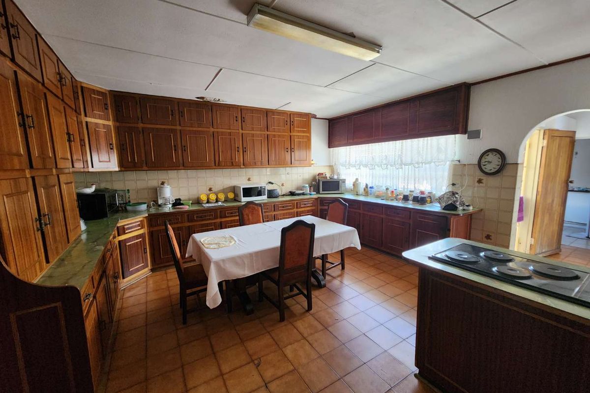 Spacious kitchen featuring extensive wooden cabinetry, tiled flooring, and a central island with a built-in cooktop, offering significant potential for modernization.