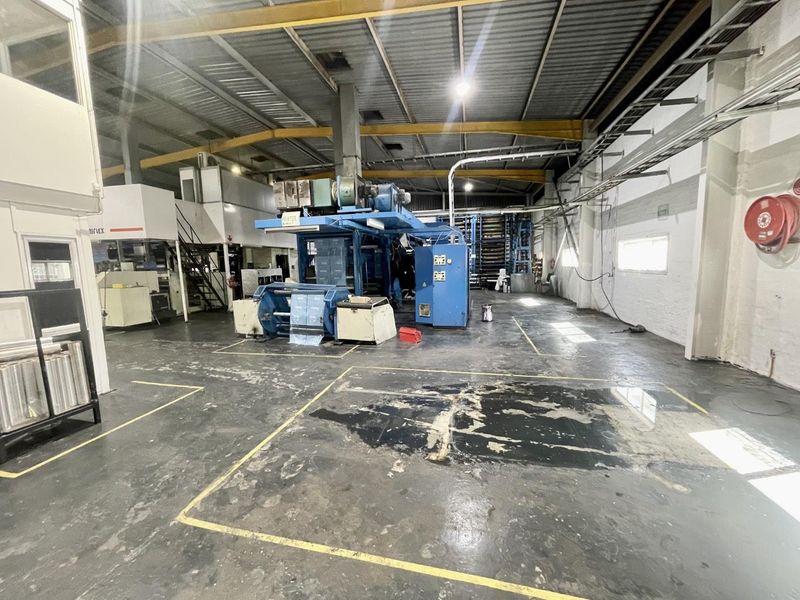 Spacious industrial warehouse area featuring high ceilings with exposed steel trusses, concrete flooring, and integrated mezzanine office space.