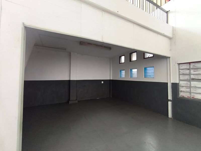 An empty industrial utility space featuring concrete flooring, fluorescent lighting, and a mezzanine level, suitable for storage or workshop use.