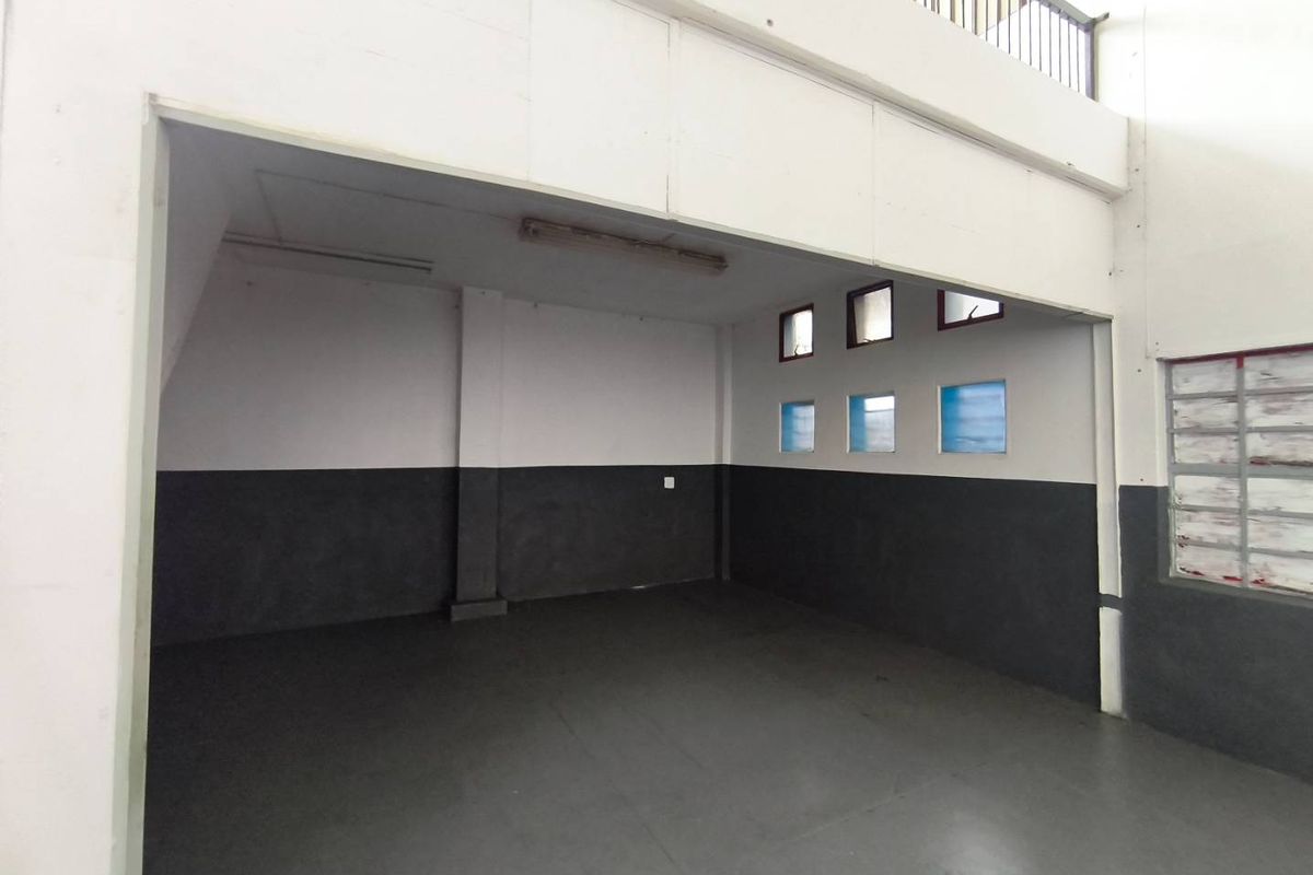 An empty industrial utility space featuring concrete flooring, fluorescent lighting, and a mezzanine level, suitable for storage or workshop use.