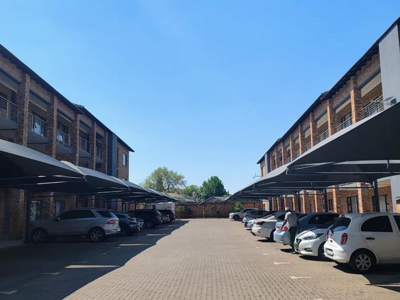 Exterior view of an apartment complex featuring a paved parking area with covered carports and multi-story brick residential buildings.