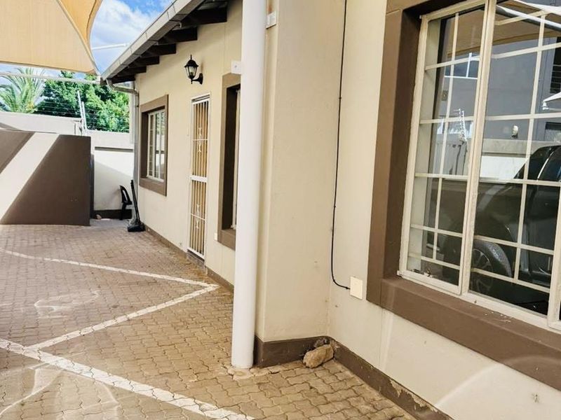 Exterior view of the townhouse front facade featuring a paved driveway, security bars on windows, and a shade sail covering the entrance area.