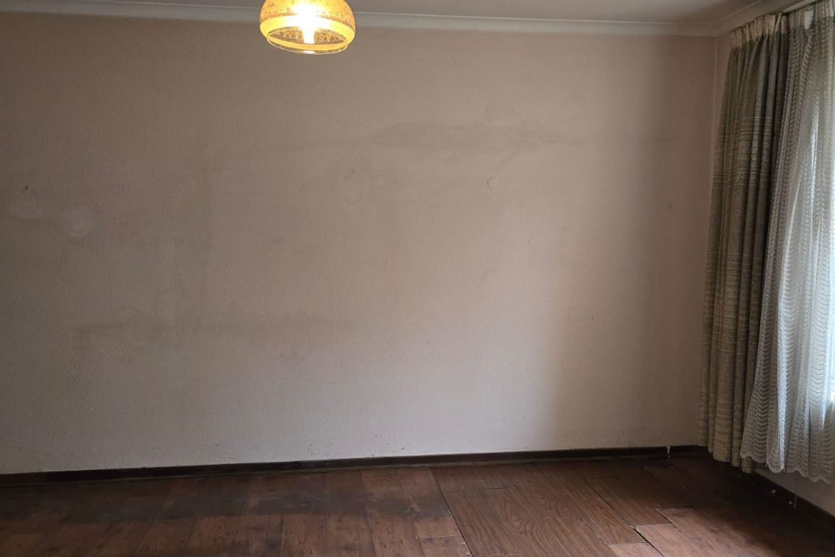 An empty living room featuring timber flooring, large windows with security bars, and a central light fixture, requiring cosmetic updates.