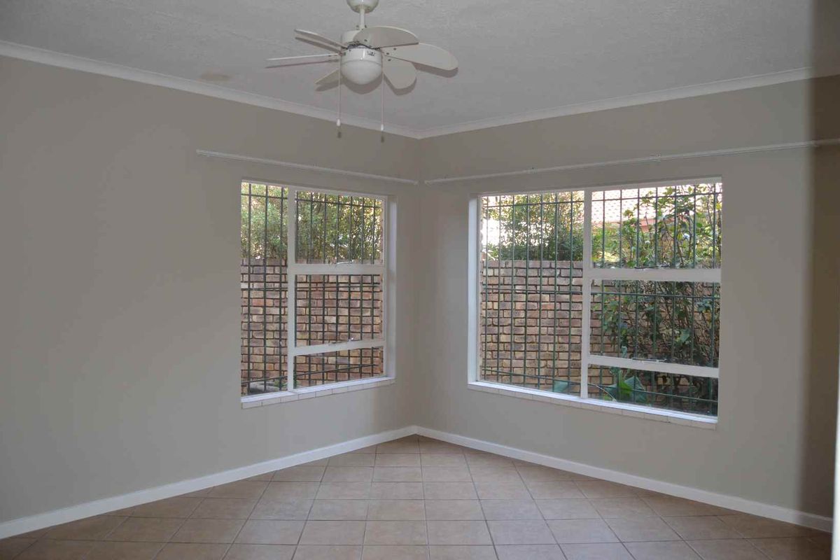 An empty bedroom featuring tiled flooring, a ceiling fan, and large windows fitted with security bars.