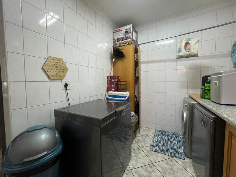 Functional laundry room featuring full-height wall tiling, durable floor tiles, and built-in cabinetry with countertop space for appliances.