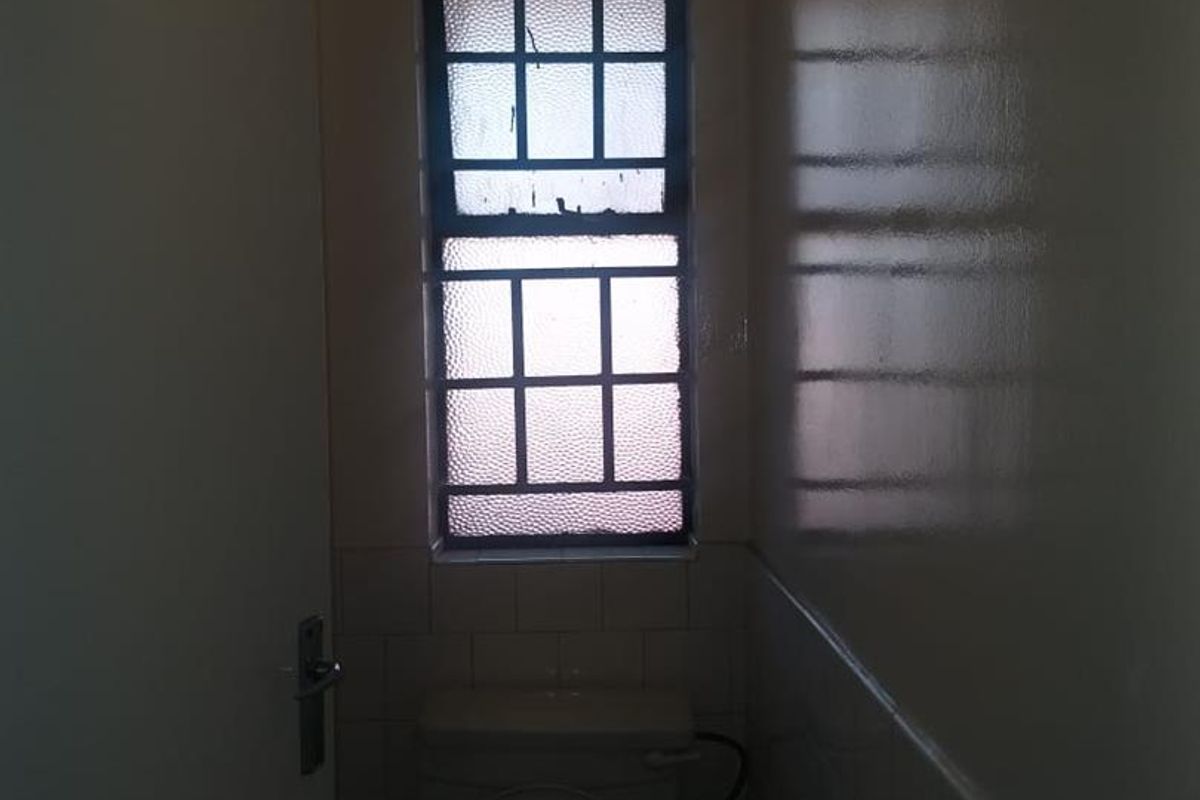 A compact, dated bathroom featuring a standard toilet and tiled walls, requiring modernization to improve its aesthetic and functionality.