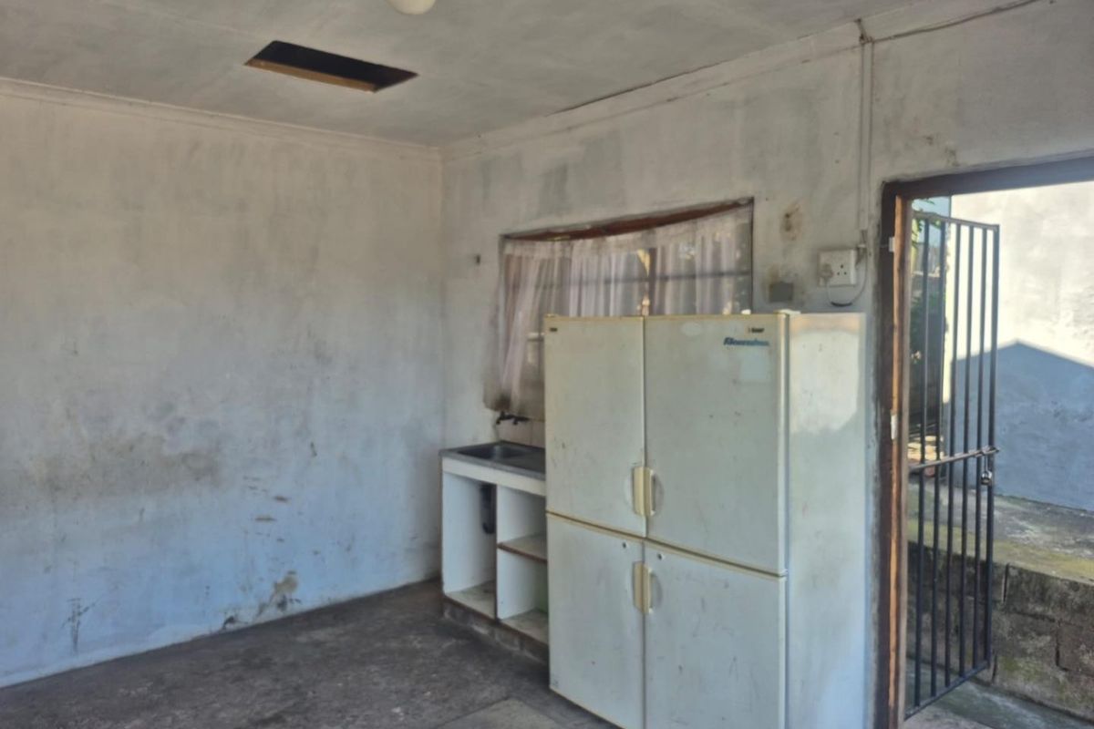 A basic, unfinished kitchen area featuring a sink and direct access to an exterior security gate, requiring significant renovation and cosmetic updates.