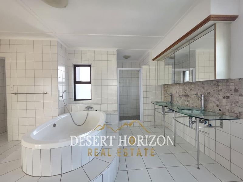Spacious bathroom featuring a built-in bathtub, a glass vanity with dual vessel sinks, and a separate shower enclosure with tiled finishes throughout.