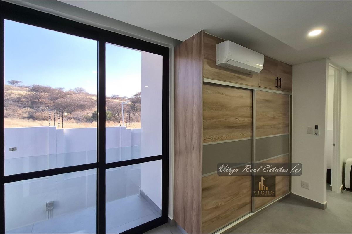 Modern bedroom featuring a large built-in wardrobe, split-system air conditioning, and floor-to-ceiling glass doors opening to an outdoor area.