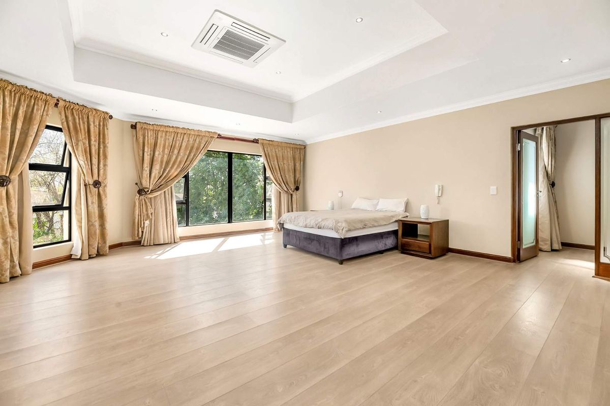 Spacious bedroom featuring light wood-look flooring, a recessed tray ceiling with integrated air conditioning, and large windows providing ample natural light.