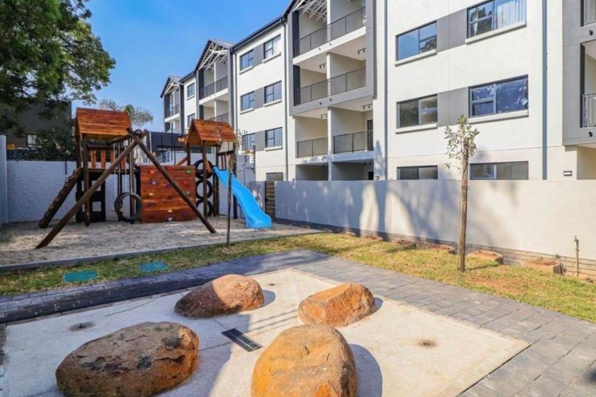 Exterior view of an apartment complex featuring a communal playground area with sand pit and landscaped garden space.