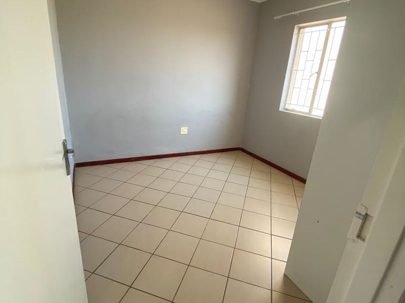 A vacant bedroom featuring neutral grey walls, tiled flooring, and a window fitted with security bars.