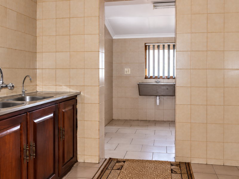 A functional scullery area featuring wooden cabinetry, double stainless steel sink, and a secondary utility sink with tiled finishes throughout.