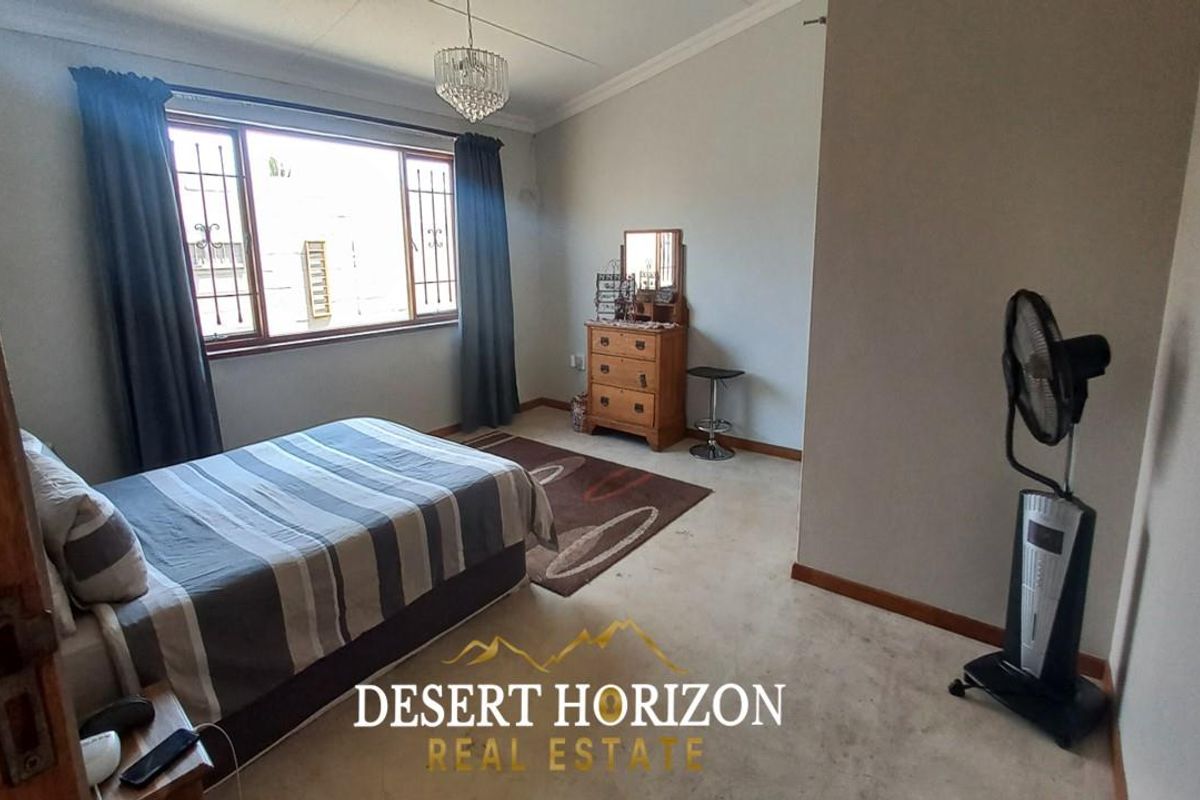 A spacious bedroom featuring large windows with security bars, neutral wall finishes, and a central light fixture.