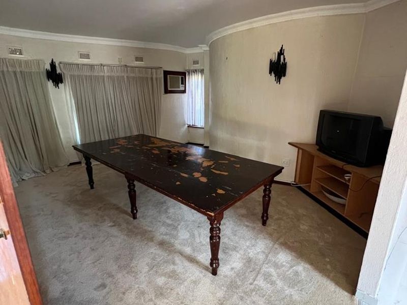 A living room featuring carpet flooring, wall-mounted lighting, and an integrated air conditioning unit, requiring cosmetic updates to improve its overall condition.