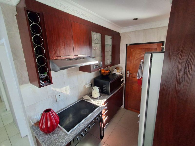 A compact kitchen featuring dark wood cabinetry, granite countertops, an electric hob, and an integrated extractor fan with tiled finishes.