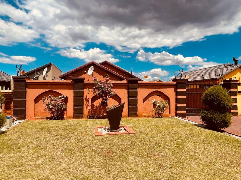A well-maintained rear garden area featuring a decorative perimeter wall with integrated electric fencing and a paved driveway entrance.