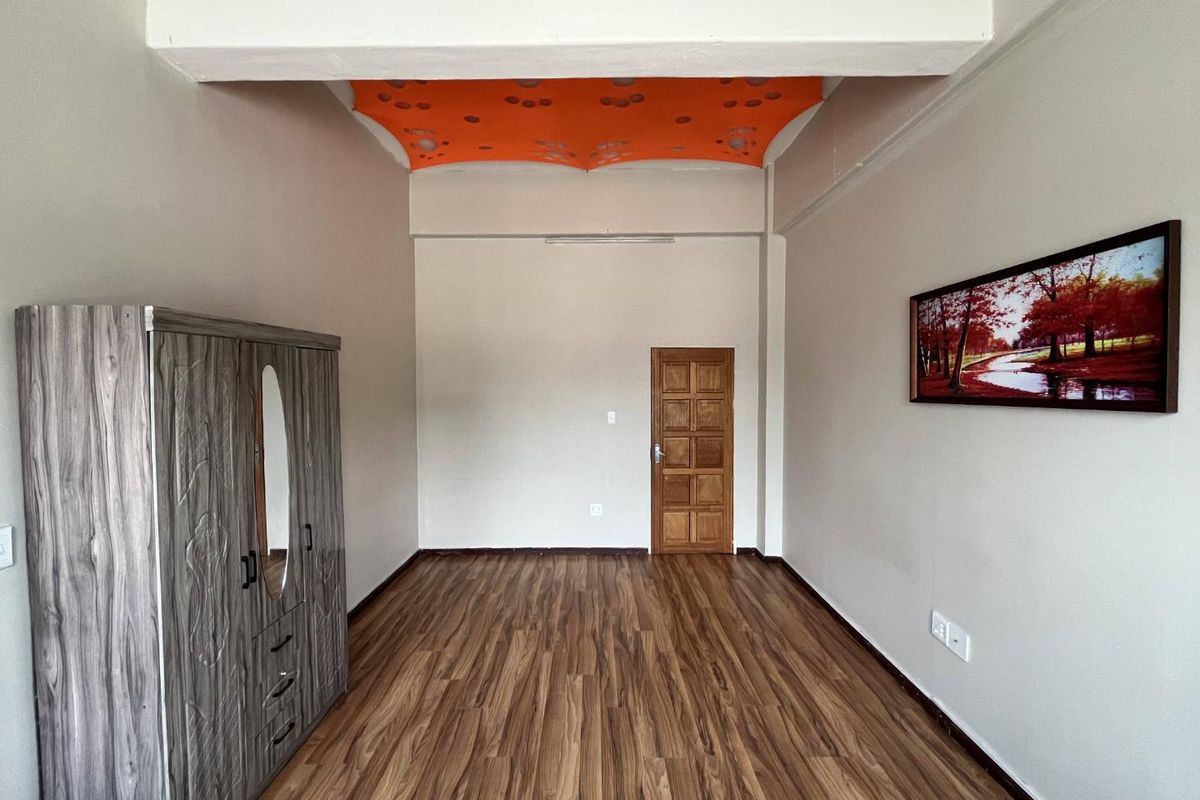 A bedroom featuring wood-look laminate flooring, a solid timber door, and a unique recessed ceiling detail.