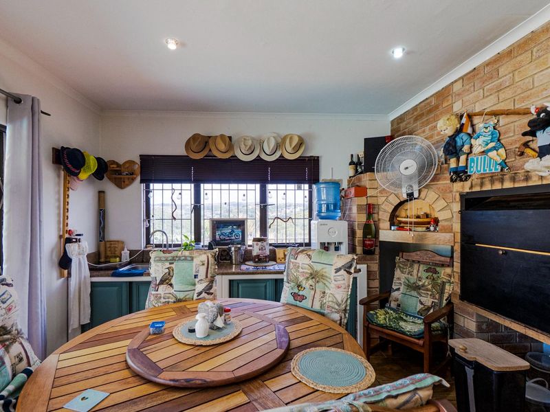 Open plan living area featuring a brick fireplace with built-in braai and a compact kitchen corner with cabinetry and sink.