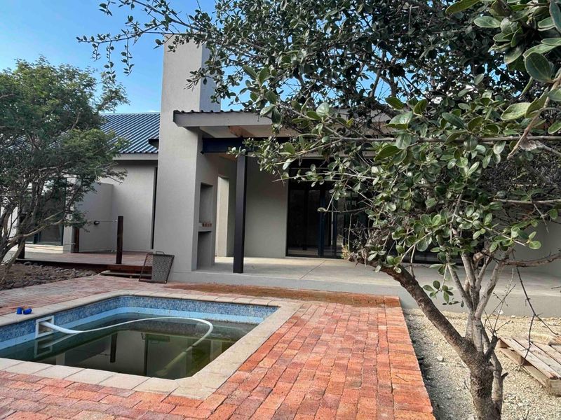 Rear exterior view featuring a swimming pool, brick paved surround, and a covered patio area with an integrated outdoor fireplace.