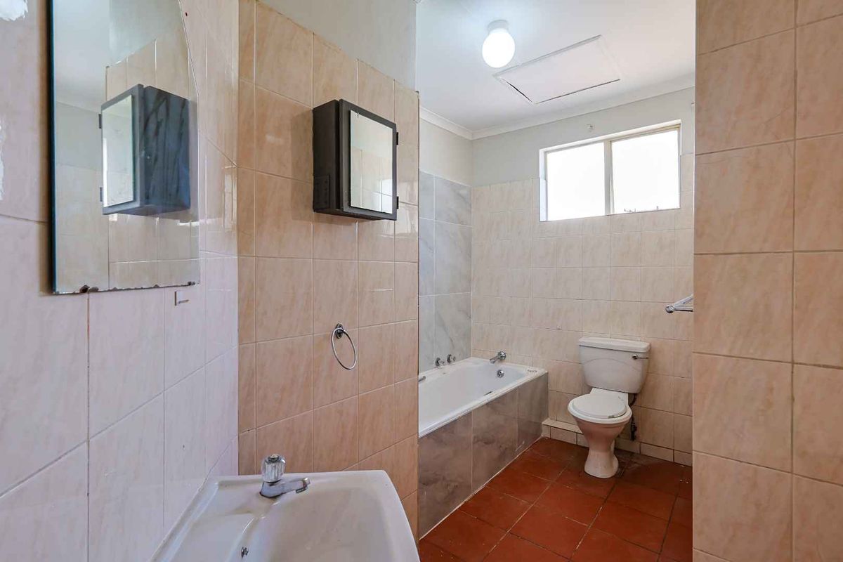 A dated bathroom featuring a built-in bathtub, pedestal sink, and toilet with ceramic wall and floor tiling.