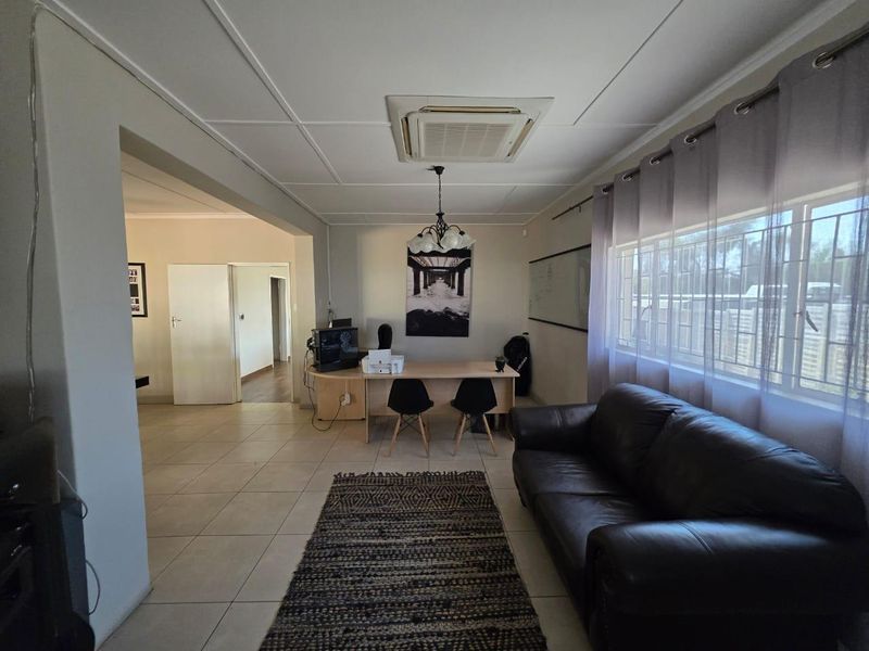 A spacious living area featuring tiled flooring, a ceiling-mounted air conditioning unit, and large windows, offering a versatile layout for relaxation or home office use.