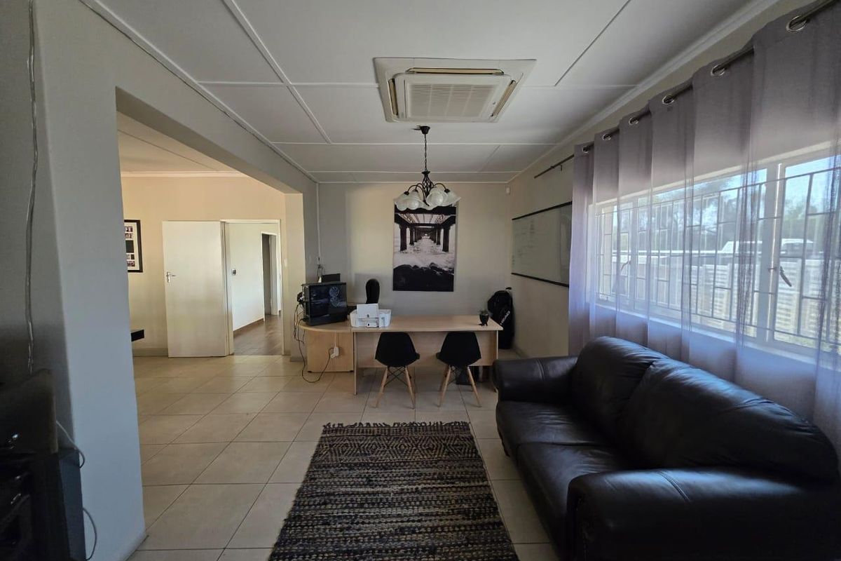 A spacious living area featuring tiled flooring, a ceiling-mounted air conditioning unit, and large windows, offering a versatile layout for relaxation or home office use.
