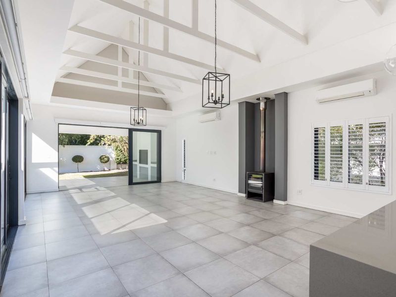 Spacious, light-filled living area featuring a vaulted ceiling with exposed rafters, a modern freestanding fireplace, and large sliding doors opening to the garden.