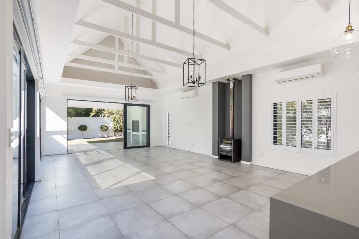 Spacious, light-filled living area featuring a vaulted ceiling with exposed rafters, a modern freestanding fireplace, and large sliding doors opening to the garden.