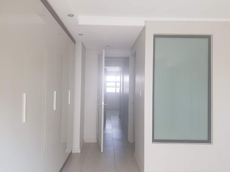 A clean, modern hallway featuring high-gloss built-in cupboards, recessed downlighting, and neutral tiled flooring, leading towards an adjacent room.