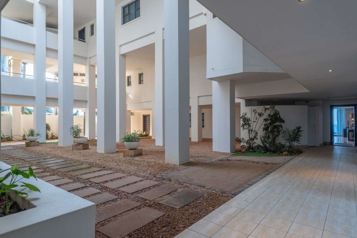 A spacious, covered outdoor courtyard area featuring structural columns, tiled walkways, and gravel landscaping within an apartment complex.