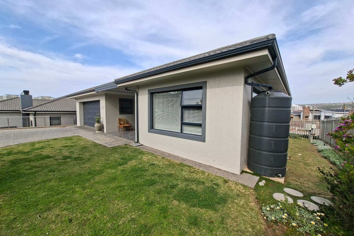 A well-maintained rear exterior view of the property featuring a paved driveway, garage access, and a large water storage tank.