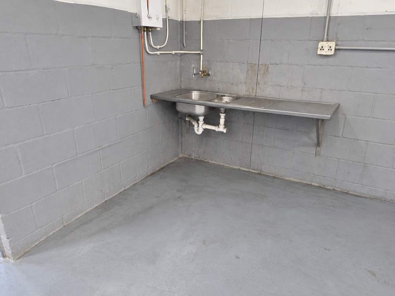 A functional industrial utility space featuring a stainless steel sink, exposed plumbing, and durable painted concrete finishes.
