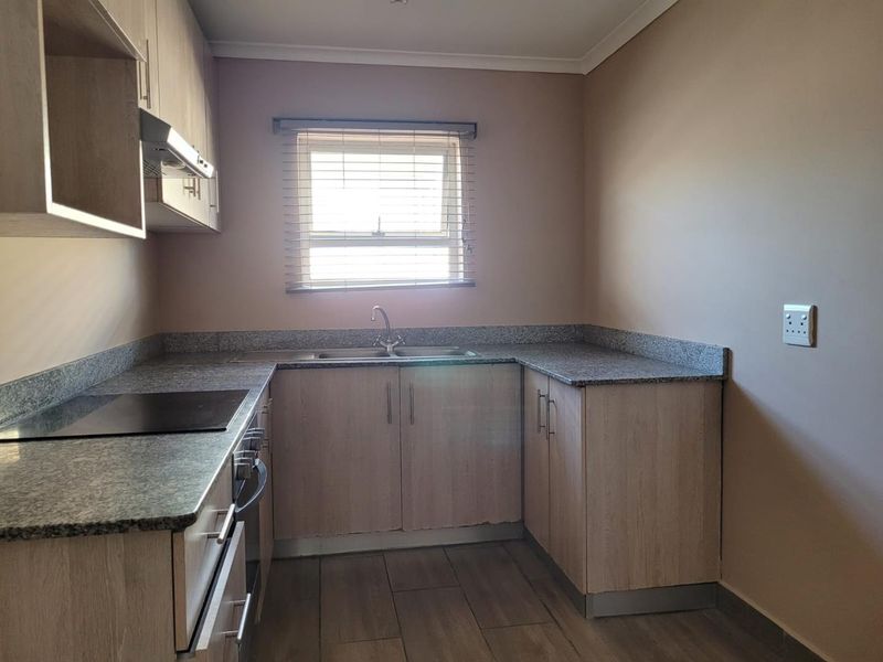 A clean and functional kitchen featuring light wood cabinetry, granite countertops, built-in oven and hob, and tiled flooring.