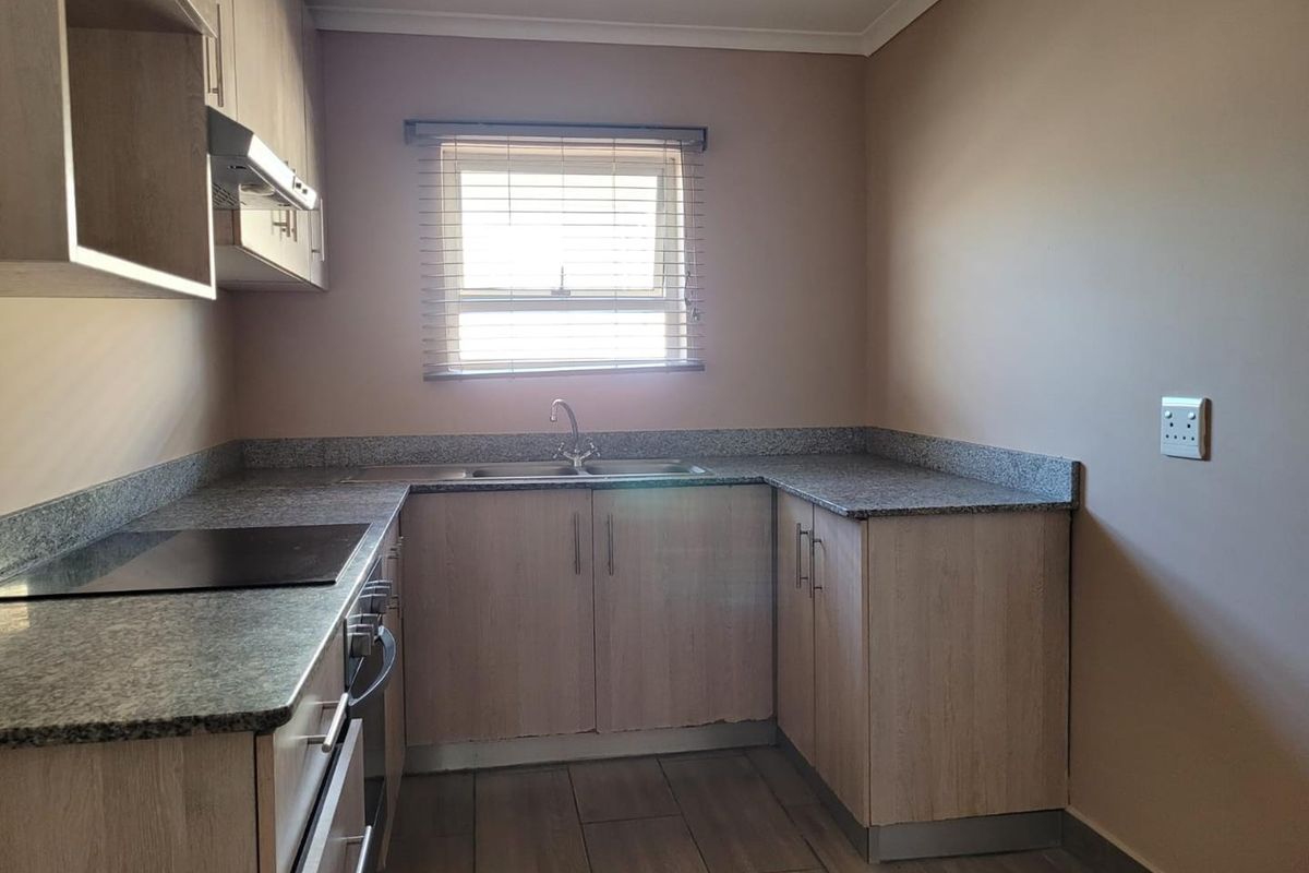 A clean and functional kitchen featuring light wood cabinetry, granite countertops, built-in oven and hob, and tiled flooring.