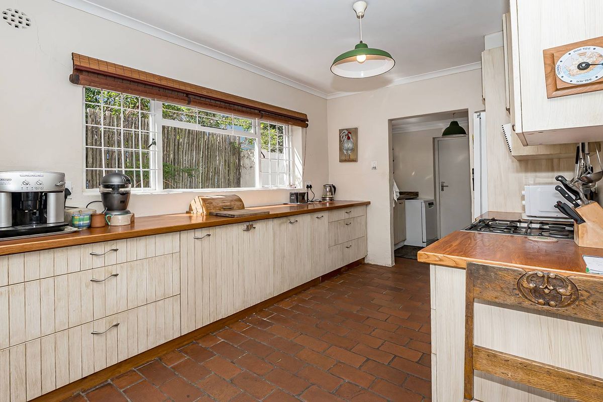 A functional kitchen featuring timber countertops, ample cabinetry, and terracotta tile flooring, with an adjacent scullery area visible through the doorway.