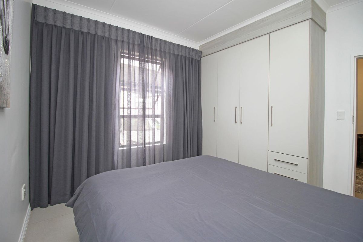 A well-maintained bedroom featuring built-in cupboards with a modern finish and neutral tiled flooring.