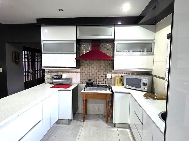 Modern kitchen featuring white high-gloss cabinetry, stone countertops, tiled splashback, and integrated extractor fan, requiring attention to the hob installation and gas connection.