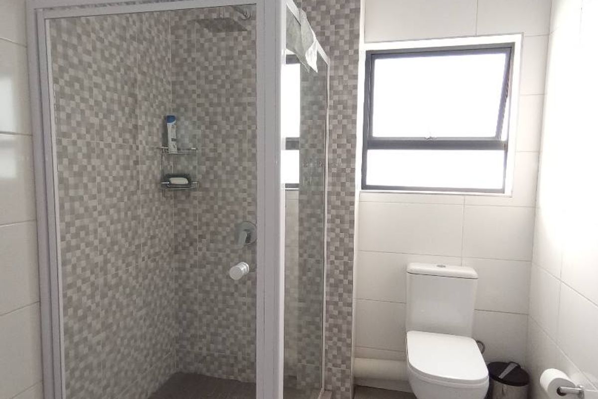 A modern bathroom featuring a glass-enclosed shower with mosaic tile accents, a white toilet, and a window for natural light.