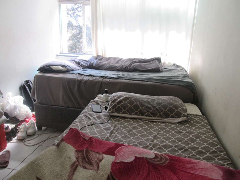 A bedroom featuring tiled flooring and a window, currently showing signs of wear and requiring cosmetic updates to improve its overall condition.