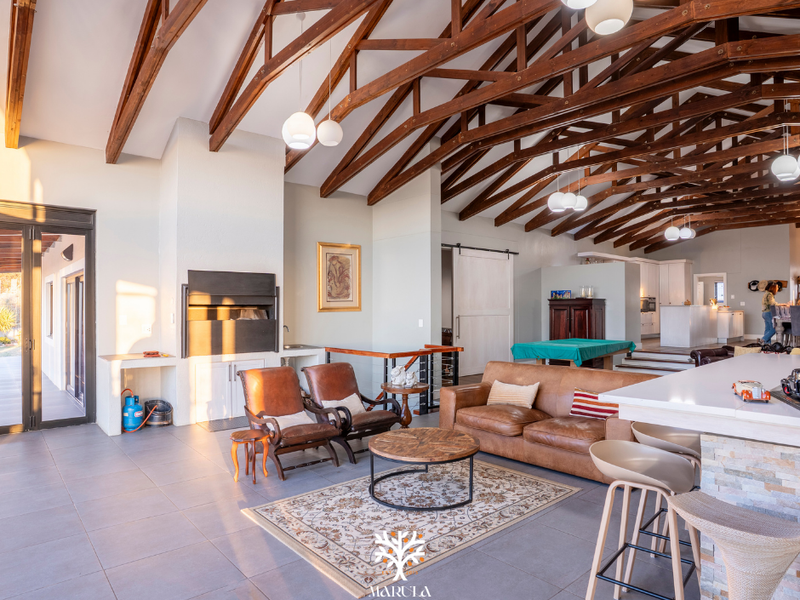 Spacious open-plan living area featuring high exposed timber trusses, a built-in fireplace, and a modern kitchen island with stone cladding.