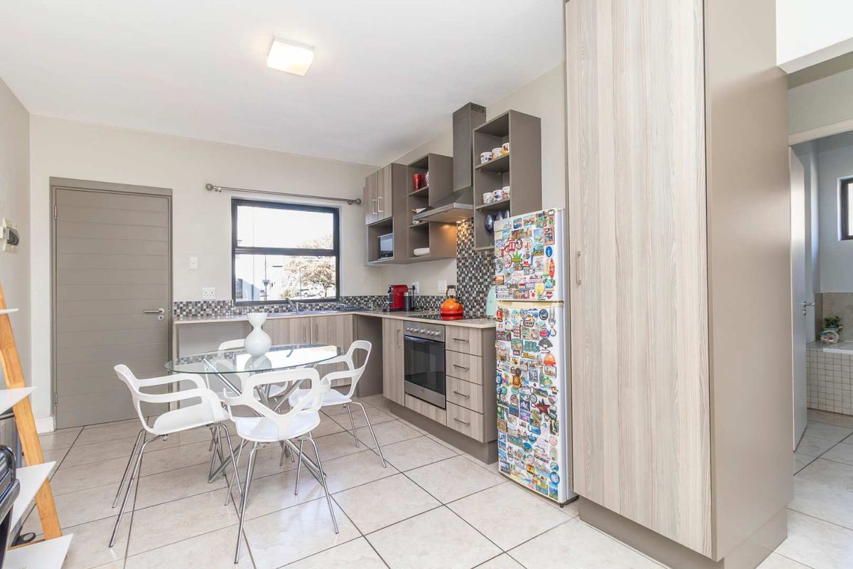 A functional kitchen featuring modern cabinetry, a mosaic tile backsplash, built-in oven and hob, and tiled flooring, with an adjacent dining area.